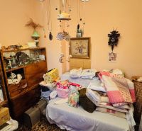 A room in a 3-room apartment with a bed, blankets, and a bookshelf with books.
