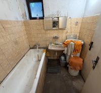 A bathroom in a family house with a bathtub, sink, and beige tiles on the walls.