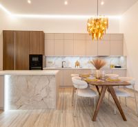 A kitchen with an island, a wooden decor floor, a dining table, and a golden chandelier.