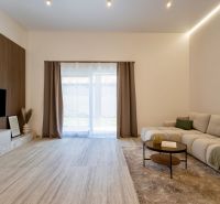 Living room of a family house with a sofa, wood-patterned floor, and a TV on the wall.