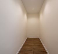 A narrow hallway in a family house with white walls and a wooden-patterned floor.