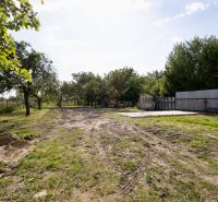 A plot of land in Zemplínska Široká with grass, trees, and a metal fence near a family house.