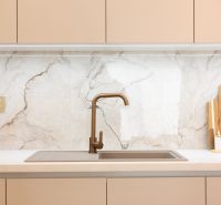 A kitchen unit with a gold faucet and marble tiles in a family house.