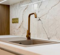 Kitchen faucet and countertop in a family house with a marble wall decor.