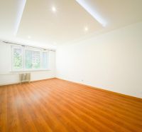 Spacious living room with wood-patterned flooring in a 3-room apartment, white walls.