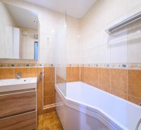 A bathroom with a bathtub and a sink in a 3-room apartment with tiles and a mirror.