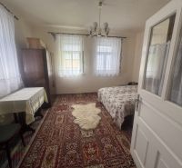 A room in a family house with a carpet, bed, table, and curtains on the windows.