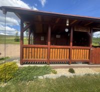 A wooden gazebo by a family house in Orlov, surrounded by a landscaped garden and a hedge.