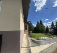 A family house in Orlov with a walkway and greenery, surrounded by trees and a blue sky.