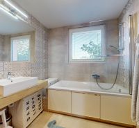 A bathroom with a bathtub, sink, decorative tiles, and a window in a 3-room apartment.