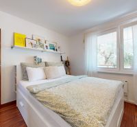 A bright bedroom in a three-room apartment with a wooden decor floor and a large window.