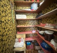 A pantry in a 2-room apartment with floral wallpaper and storage shelves.