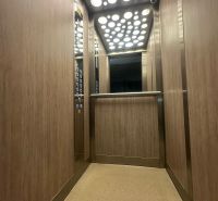 The interior of an elevator in a 2-room apartment with wooden decor on the walls.