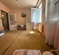 Living room in a two-room apartment with a carpet, open window, furniture, and paintings.