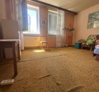 A room in a 2-room apartment with a carpet, an open window, and simple furniture.