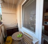 A balcony of a 3-room apartment with a wooden table and chairs, next to the kitchen window.
