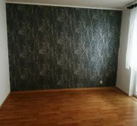 A room in a 3-room apartment with a wooden-patterned floor and patterned wallpaper.
