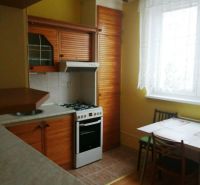A kitchen in a 3-room apartment with a wooden decor floor, a dining table, and a stove.