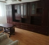 Living room with dark wooden furniture and wood-patterned flooring in a three-room apartment.
