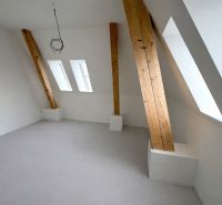 An attic room with a white wall and wooden beams in a 2-room apartment.