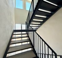 A staircase in a 2-room apartment with black railings and large windows.
