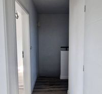 A hallway in a family house with white walls and a wooden-patterned floor.