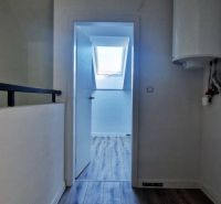A hallway in a family house with a wooden decor floor, a skylight in the background.