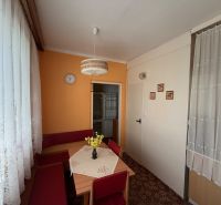 A kitchen in a 2-room apartment with an orange wall, a carpet, and lace curtains.