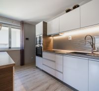 A kitchen in a family house with white cabinets, a wooden-patterned floor, and a window.