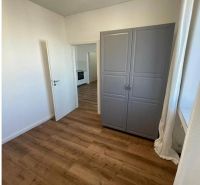 A room in a 3-room apartment with a wooden decor floor, a gray wardrobe, and a window.