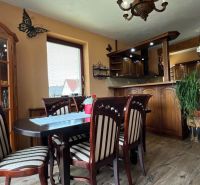 Dining area with chairs and a table, kitchen unit, floor with wood decor.