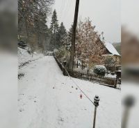 A snowy street in Horné Otrokovce with a family house and fencing.