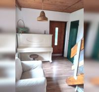 Interior of a family house with a white piano, wooden decor flooring, stairs, and wooden ceiling.