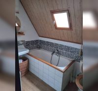 Bathroom with a bathtub and sloped ceiling, wooden decor, mosaic tiles, window.