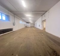 The interior of a warehouse with a concrete floor and white walls, fluorescent lighting.