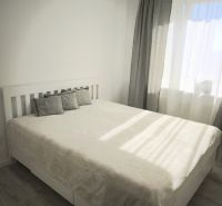 Bedroom with a bed and wooden decor flooring in a 2-room apartment, light curtains.