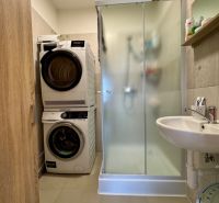A bathroom in a 3-room apartment with a shower, washing machine, and dryer.