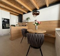 A kitchen in a family house with a wooden ceiling, a floor with a wooden decor, and stylish seating.