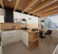 A kitchen in a family house with a wooden decor floor, wooden beams, and a dining table.
