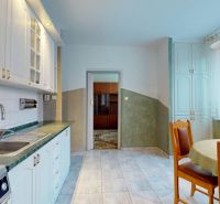 A kitchen in a 3-room apartment with a white kitchen unit and a dining table, flooring with a decor.