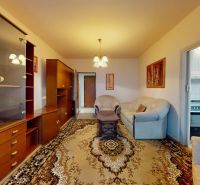 Living room of a three-room apartment with carpet flooring, a sofa, and a built-in wardrobe.