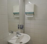 A sink in offices with a soap dispenser and a mirror on the wall.
