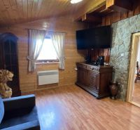 The interior of a cabin with a wood-patterned floor, a television, and a stone wall.