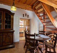 Interior of a cottage with a wooden staircase, dining table, and rustic cabinet.