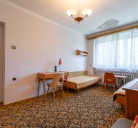 A room in a 3-room apartment with a carpet, furniture, and a large window.