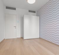 A bright room with parquet floors, a white wardrobe, and patterned wallpaper on Továrenská Street.