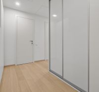 A hallway with a wooden floor and a white built-in wardrobe, located on Továrenská Street.