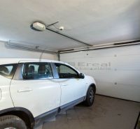 A car parked in the garage of a family house with white walls and a tiled floor.