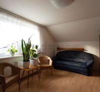 Living room with wooden floor decor, dark sofa, and wicker chairs in a family house.