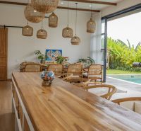 Interior of a villa with wood-patterned flooring, wicker light fixtures, and a pool.